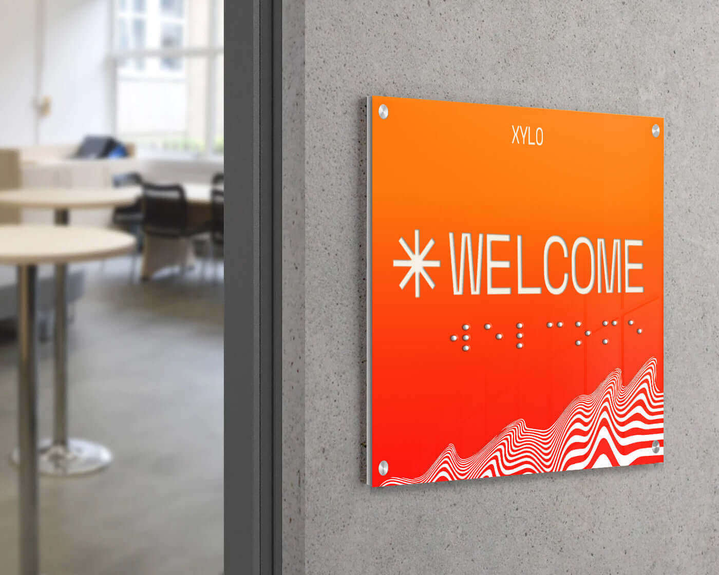 Modern 'WELCOME' sign in orange with braille, displayed in a contemporary office environment.